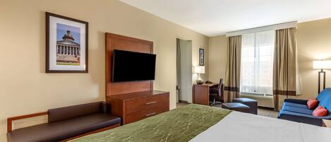 Habitación de hotel con una cama grande, un escritorio, una silla, un televisor y un cuadro en la pared.
