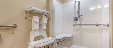 Un baño accesible para personas con movilidad reducida, con ducha, barras de apoyo, un asiento y un perchero.