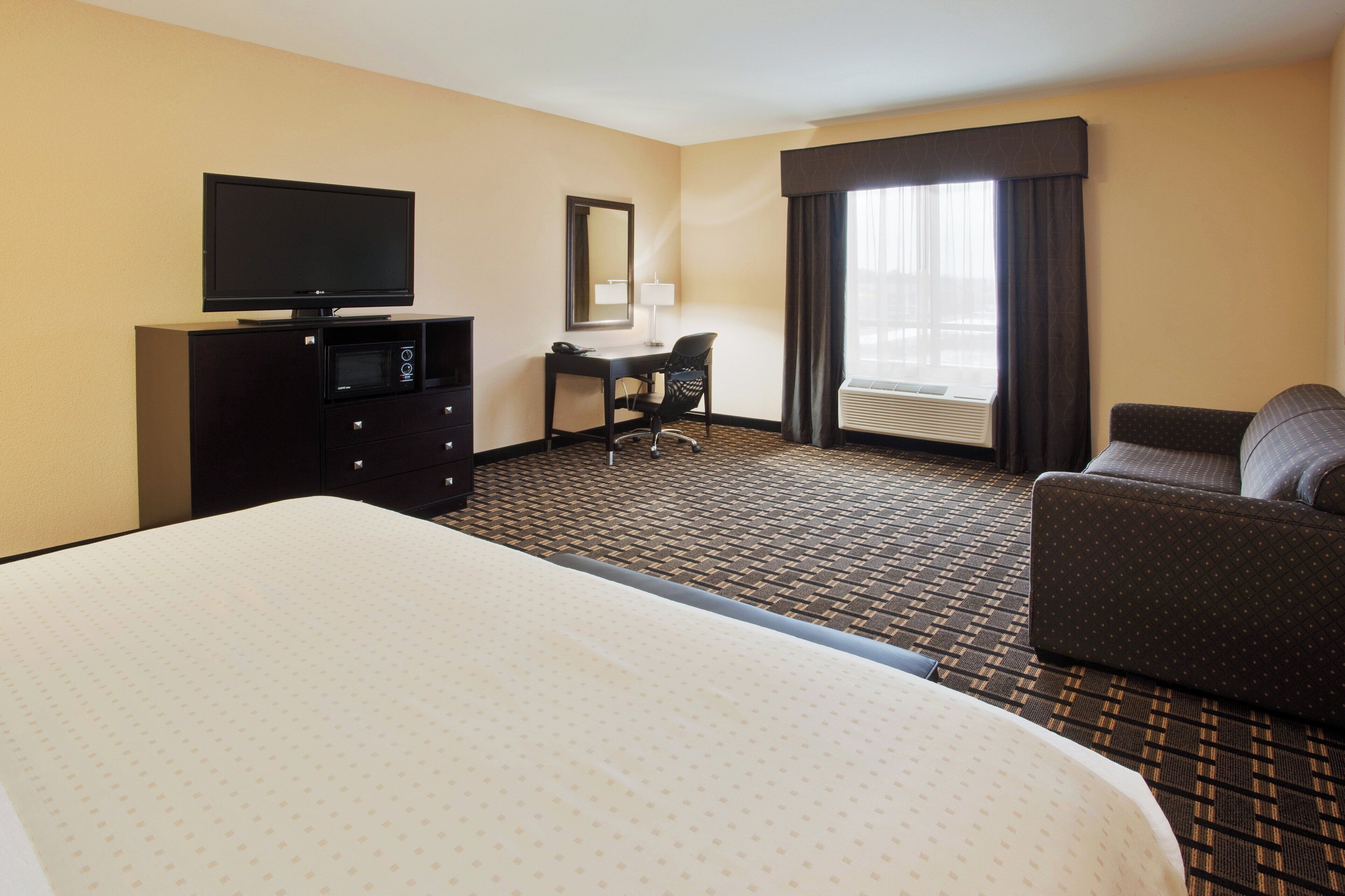 A hotel room with a bed, a desk, a chair, a television, and a window with curtains.