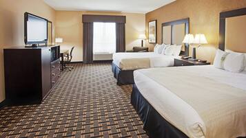 A hotel room with a large bed, a smaller bed, a desk, a chair, a television, and a window with curtains.