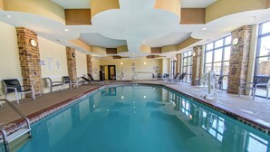 An indoor swimming pool with clear water, surrounded by lounge chairs and a stone wall.