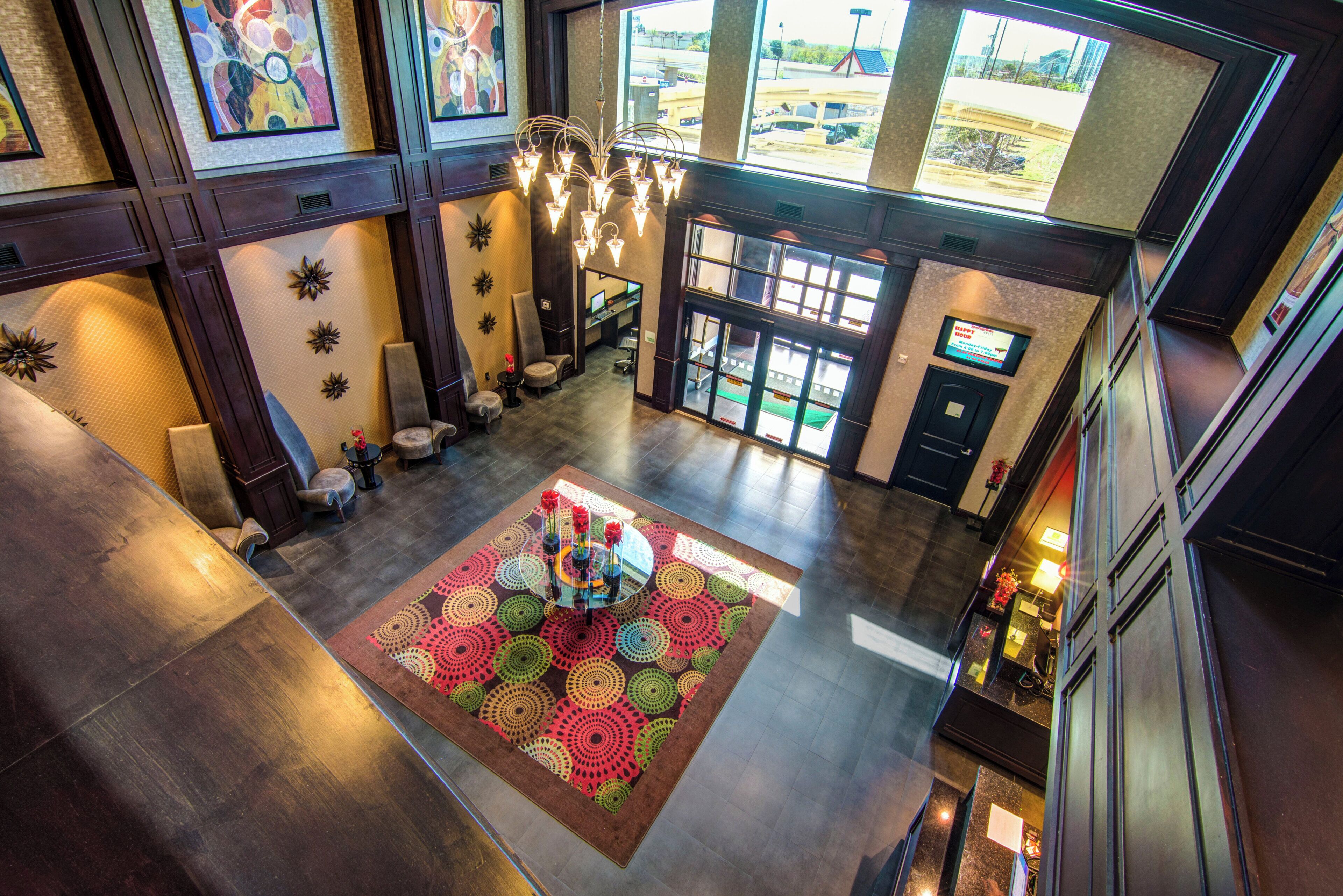 A spacious lobby with a central area rug, seating arrangements, and a view of the parking area through large windows.