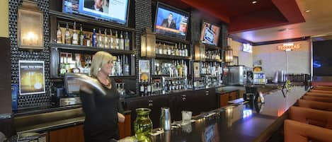 A bar area with multiple screens displaying news, a well-stocked bar, and a Texan-themed sign.