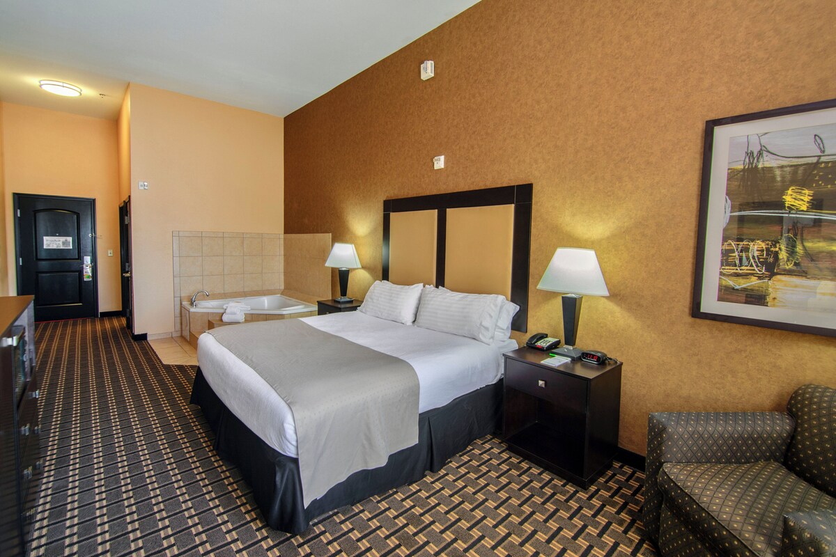 Habitación de hotel con cama, mesitas de noche, escritorio, silla, baño y un cuadro en la pared.