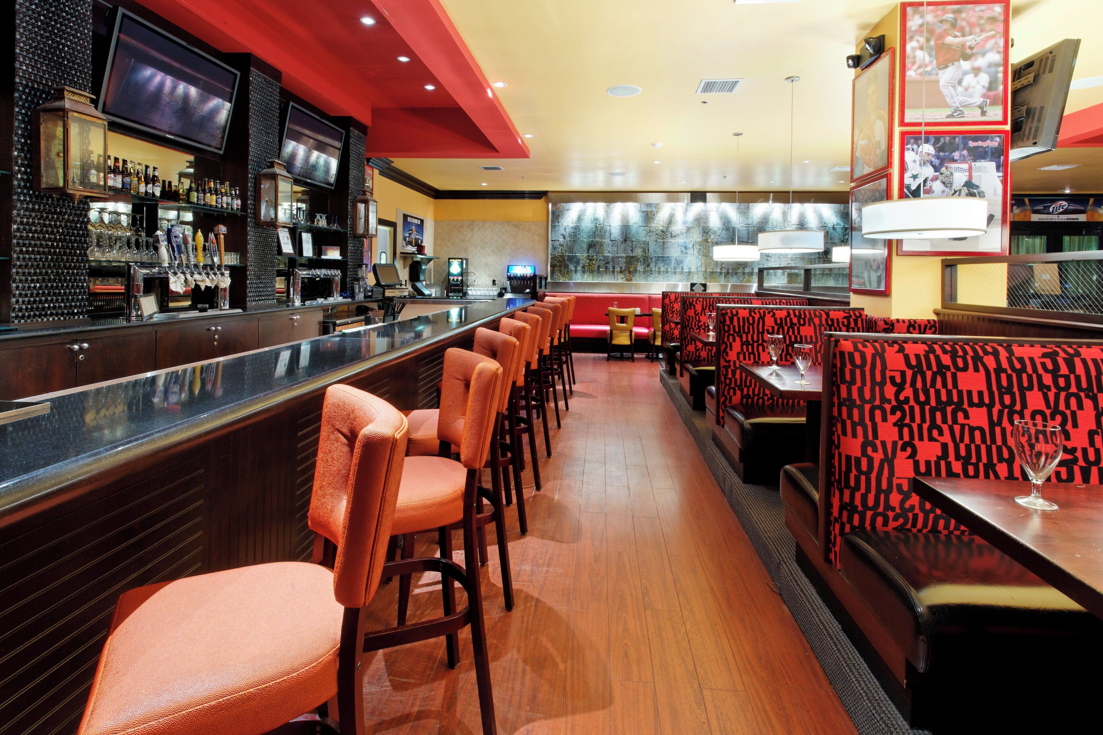 A bar area with a long counter, multiple TVs, and a variety of bottles.
