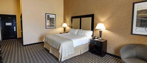 A hotel room with a bed, two bedside lamps, a chair, a door, and a framed picture on the wall.