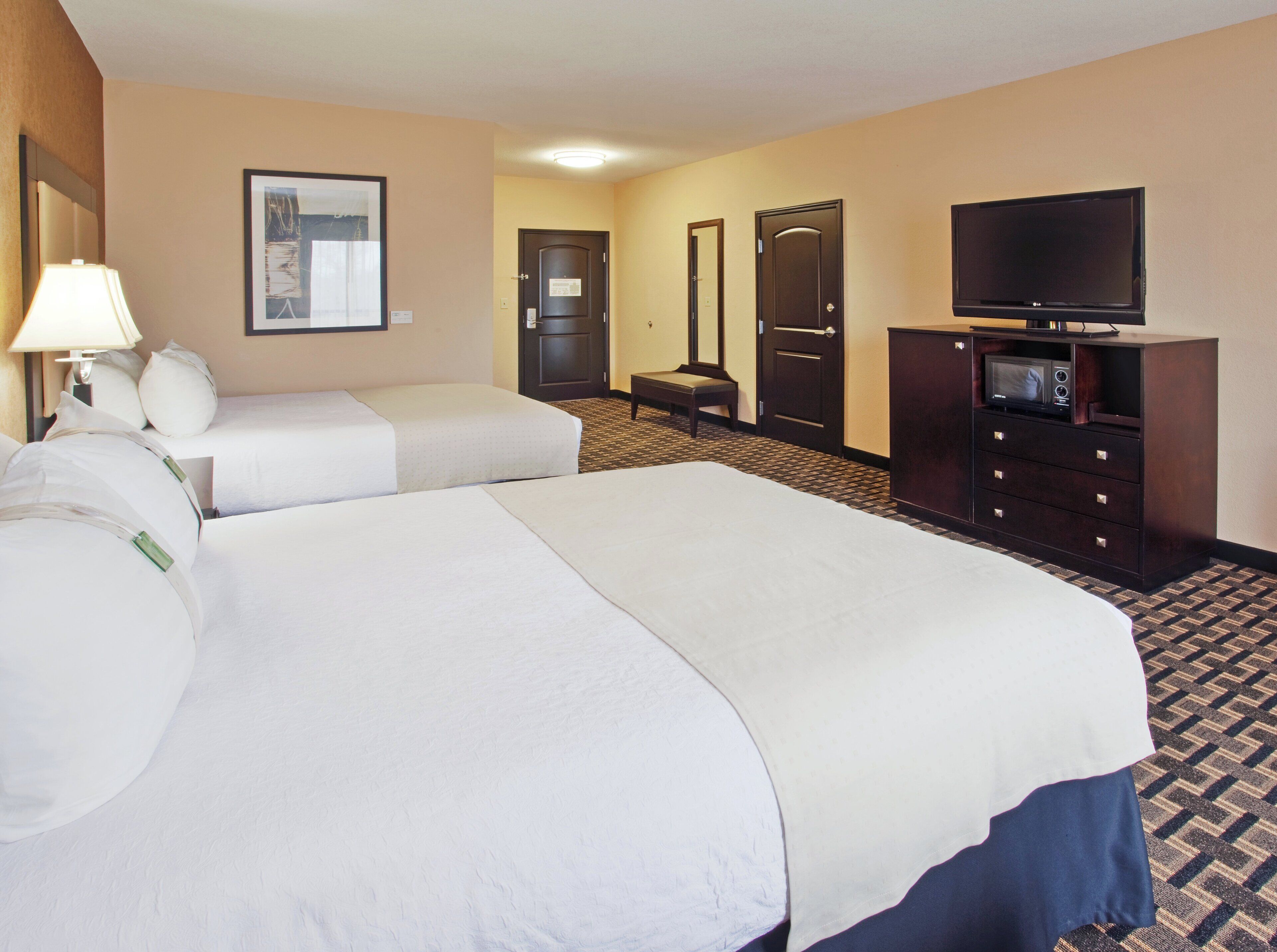 A hotel room with two beds, a television, a desk with a computer, and a mirror.