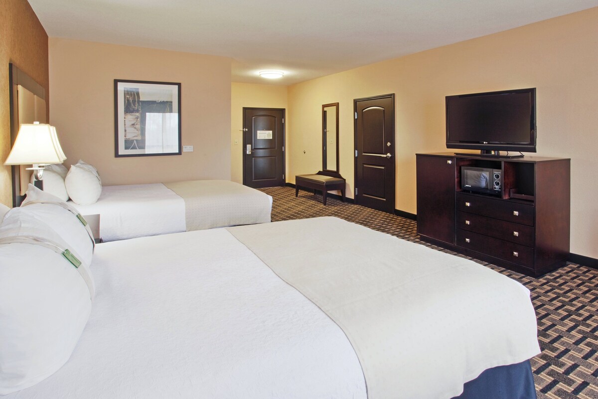 Habitación de hotel con dos camas, un televisor, un escritorio con ordenador y un espejo.