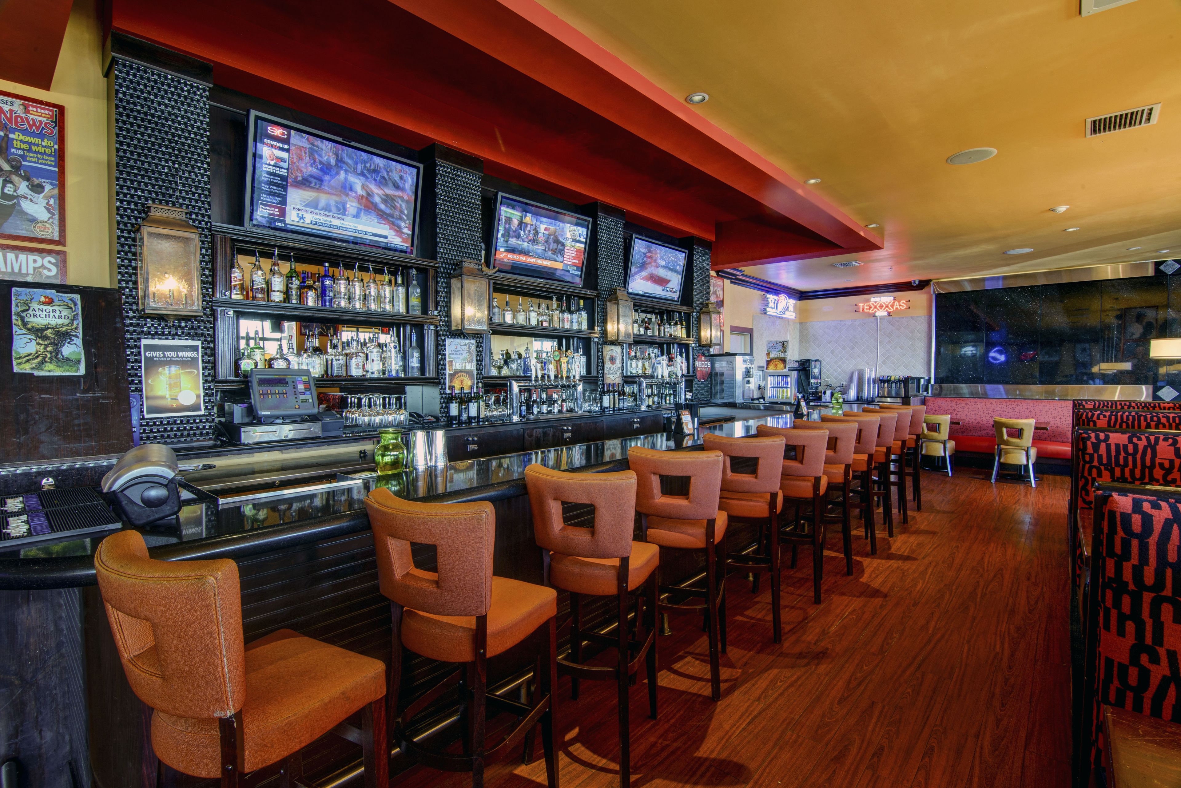 A bar area with multiple TVs, a bar counter, and several bar stools.