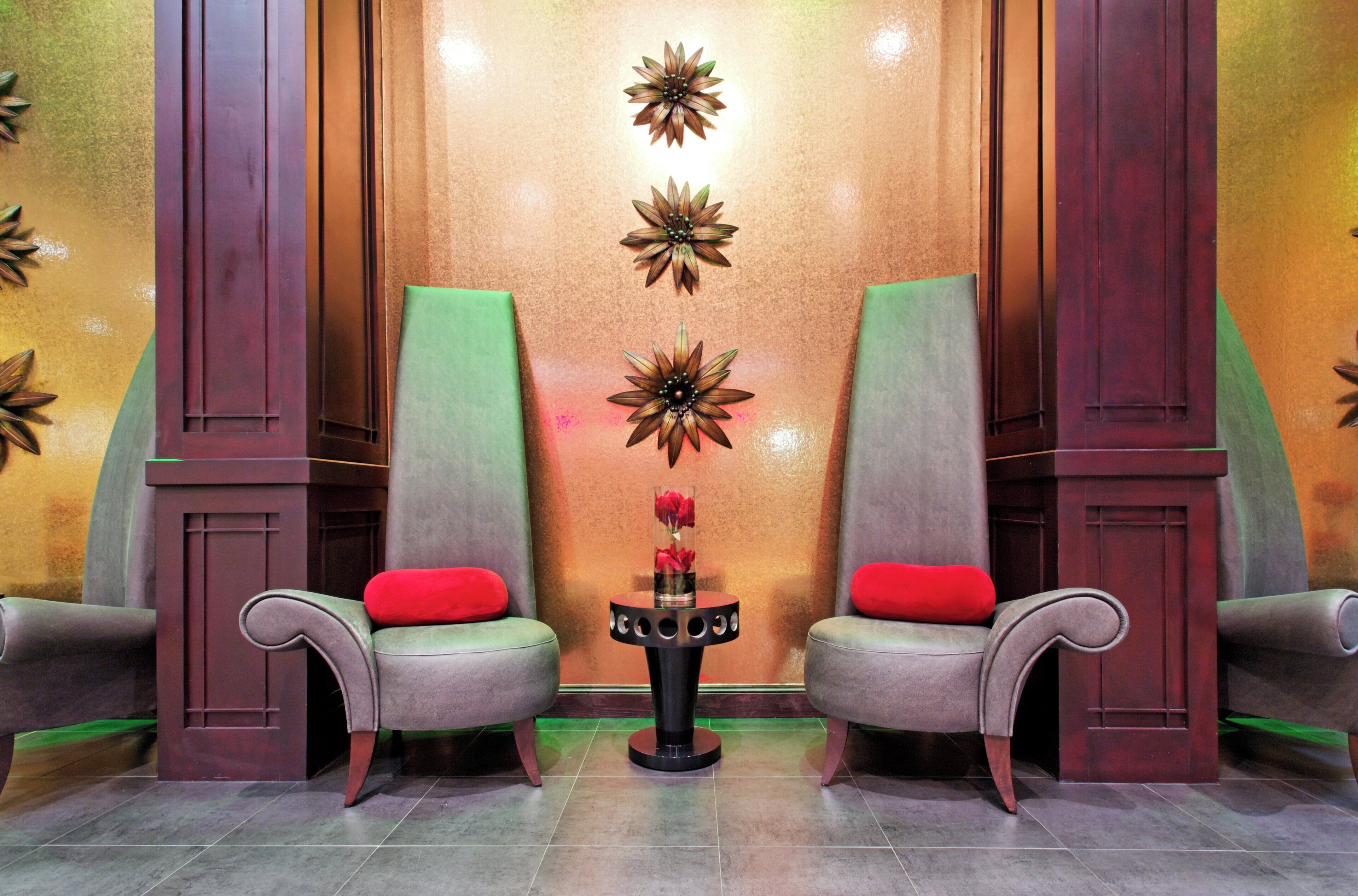 A lobby with two armchairs, a small table with a vase of flowers, and decorative wall panels.