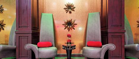 A lobby with two armchairs, a small table with a vase of flowers, and decorative wall panels.