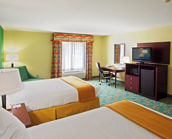 Quarto de hotel com duas camas, uma escrivaninha com computador, televisão e janela com cortinas.