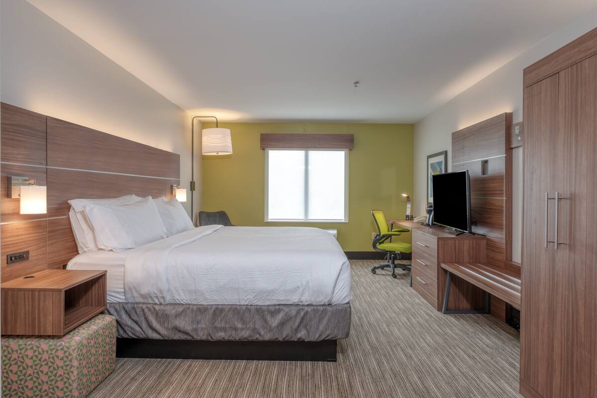 A hotel room with a large bed, a desk with a chair, a TV, and a wardrobe.