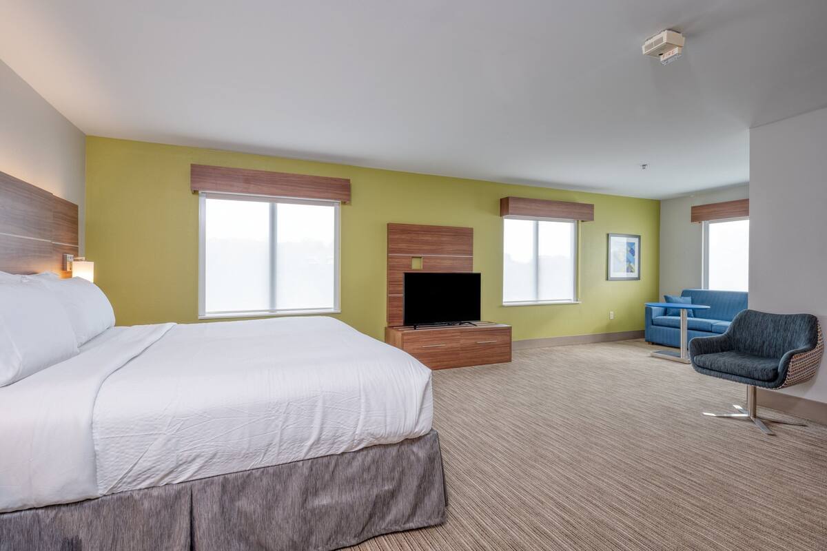 A hotel room with a large bed, a television, a desk, a blue armchair, and a sofa.