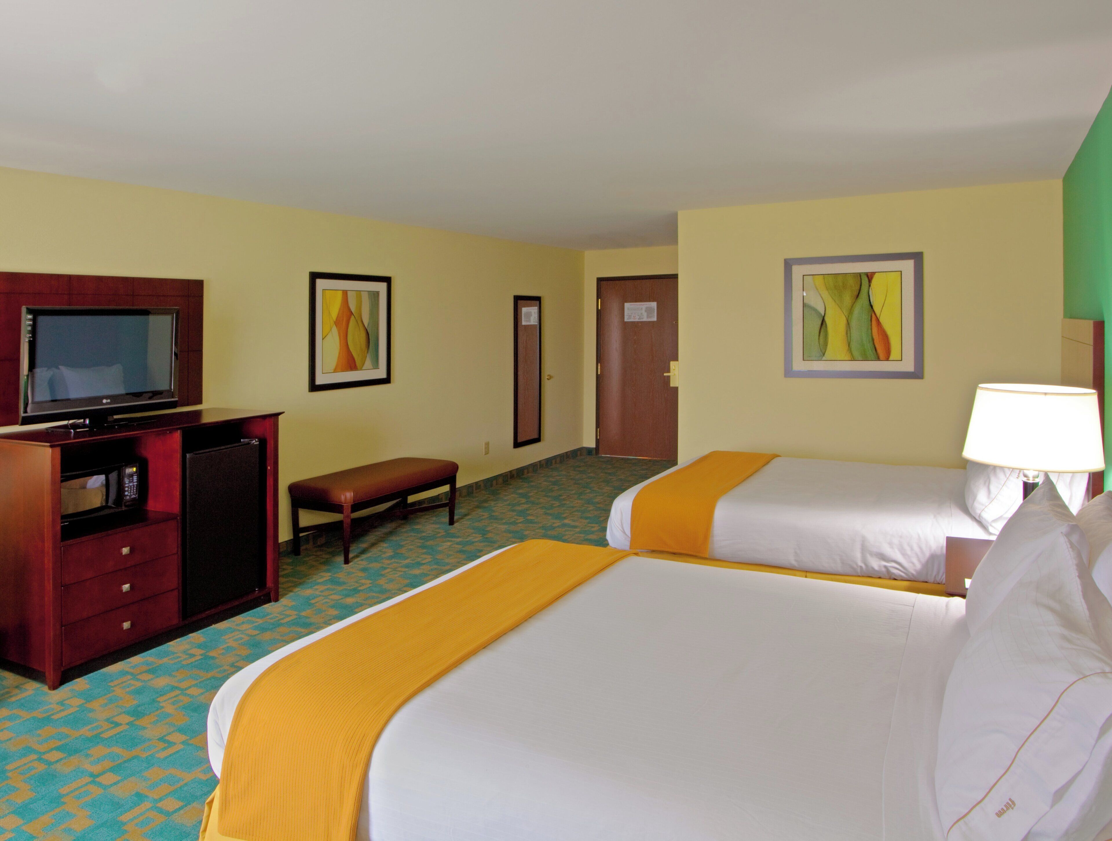 Habitación de hotel con dos camas, televisión, escritorio y un banco.