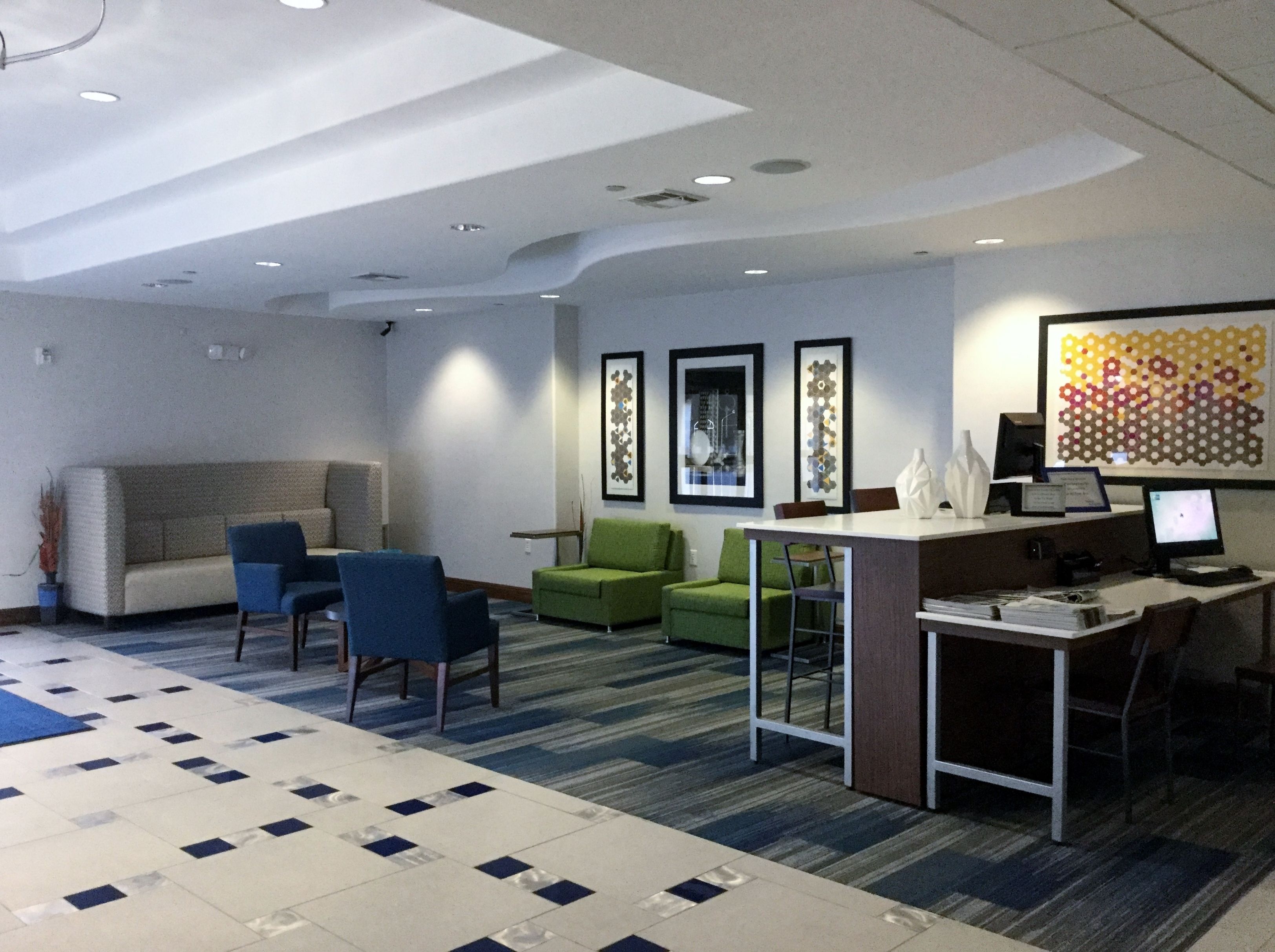 Un hall d’hôtel moderne, avec un canapé, des fauteuils, un bureau et des œuvres d’art accrochées aux murs.