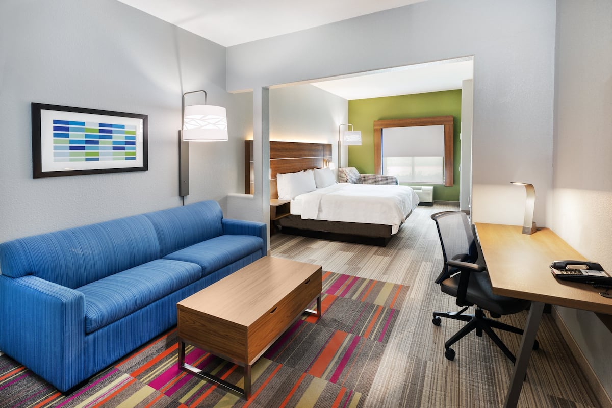A hotel room with a blue sofa, a wooden coffee table, a desk with a telephone, and a bed with white bedding.