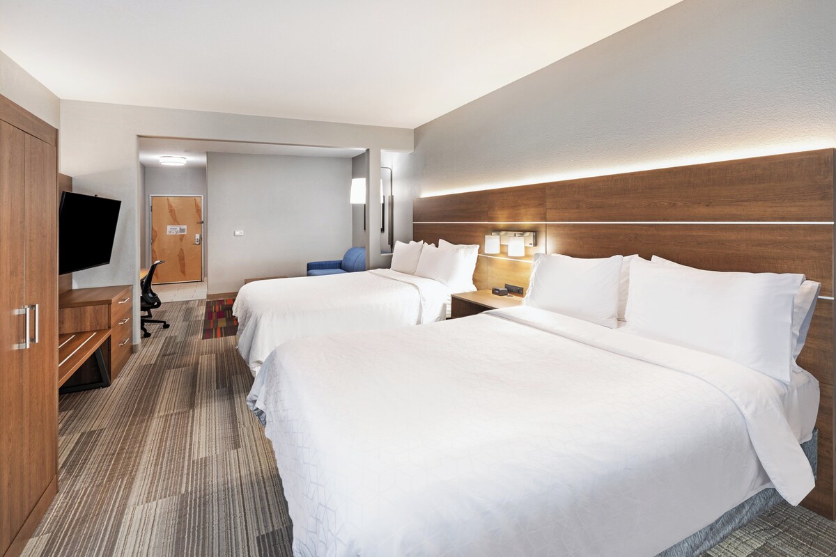 A hotel room with two beds, a desk, a chair, a TV, and a wooden headboard.