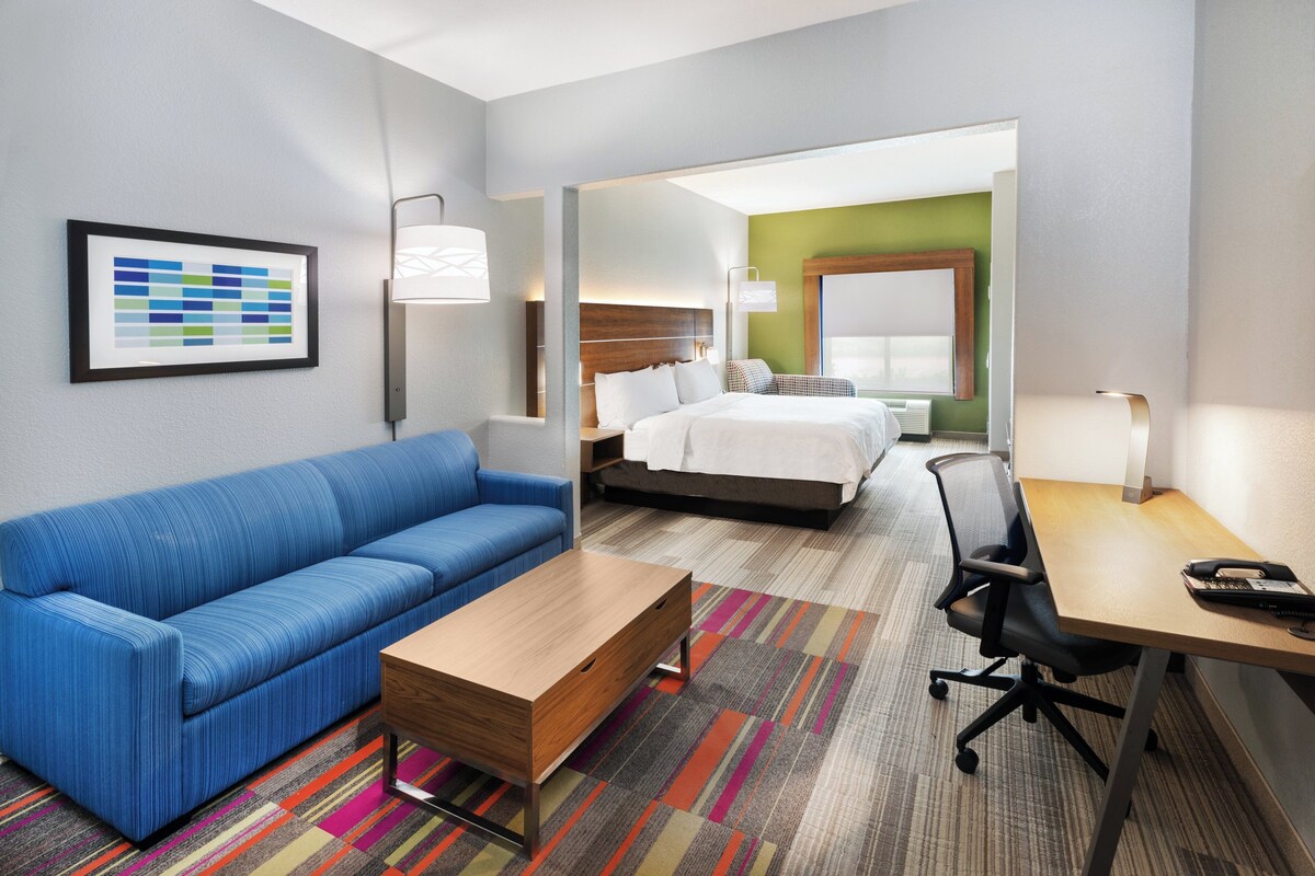 A hotel room with a blue sofa, a wooden coffee table, a desk with a telephone, and a bed with white bedding.