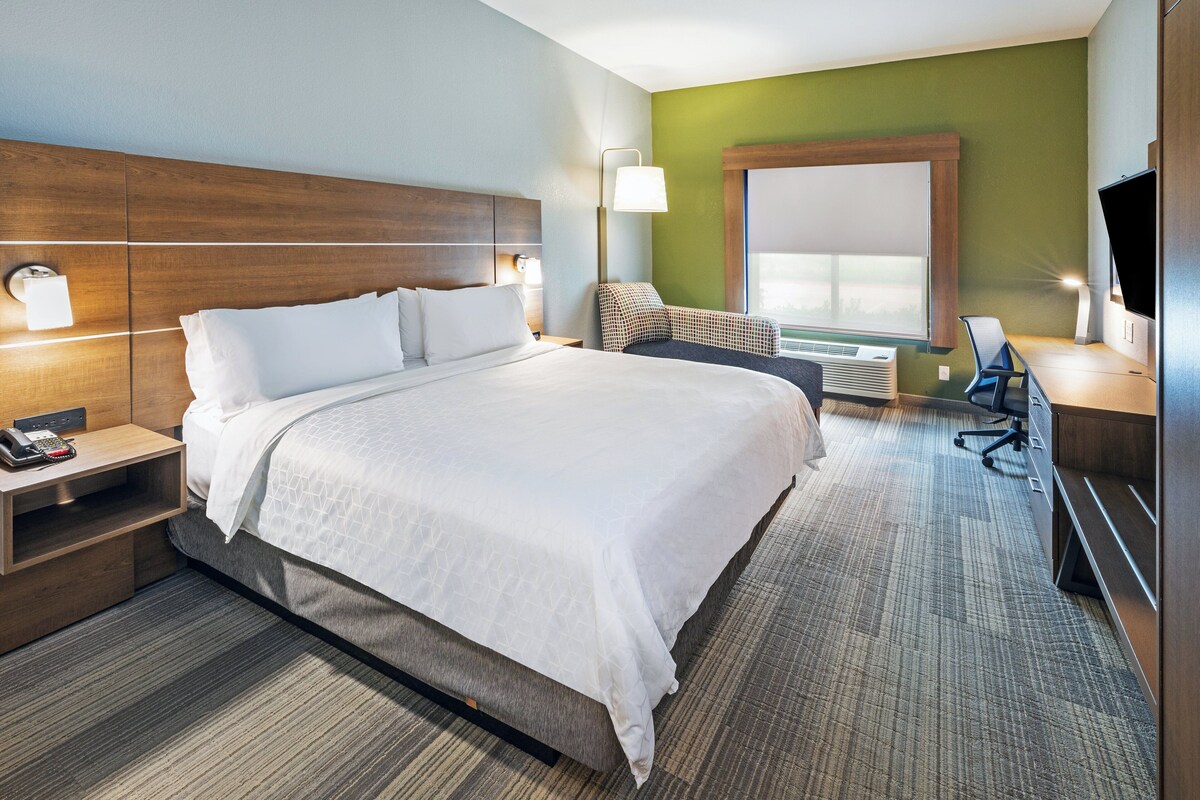 A hotel room with a large bed, a desk with a chair, a flat-screen TV, and a window with a view.