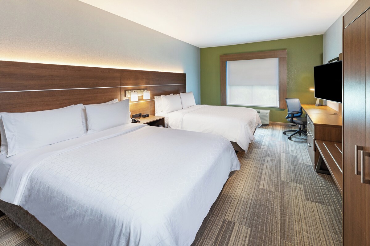 A hotel room with two beds, a desk with a chair, a television, and a large window.