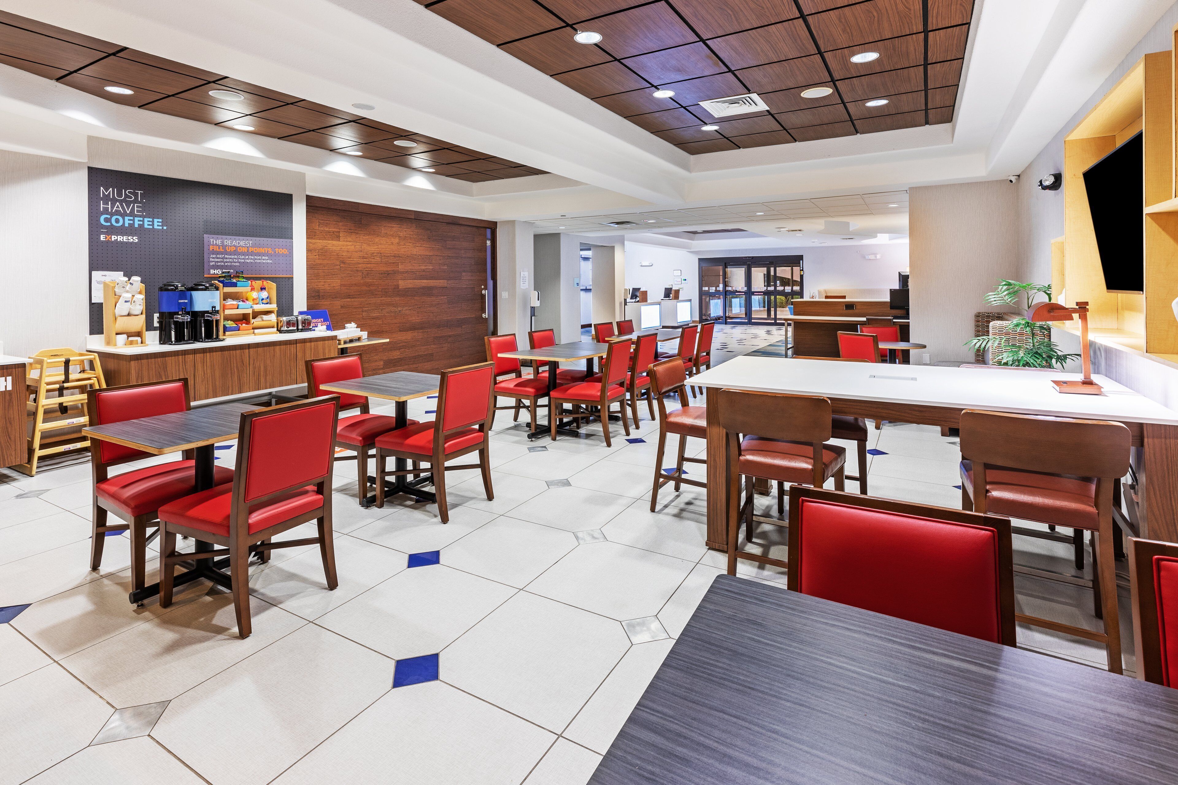 A modern hotel lobby with a coffee station, seating areas, and a reception desk.