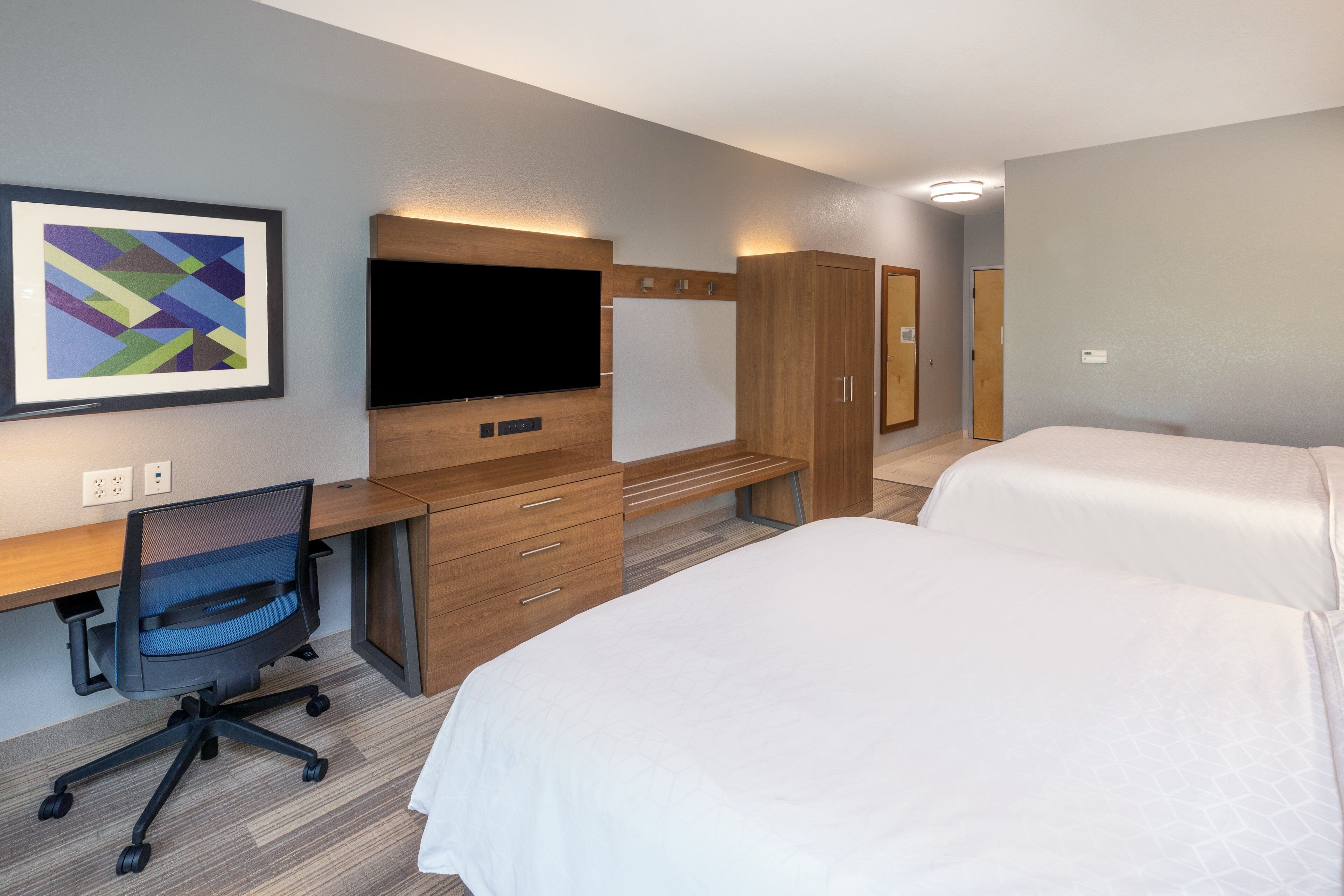 Habitación de hotel con escritorio, silla, dos camas, televisor y un cuadro en la pared.