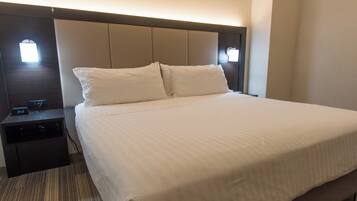 A hotel room with a large bed, a nightstand, and a wall-mounted light.