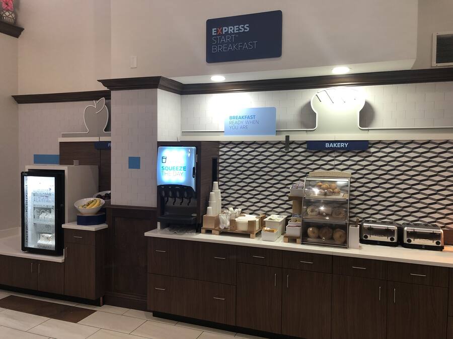 A breakfast area with a sign for 'Express Start Breakfast', a beverage dispenser, a bakery section, and a refrigerator with a yogurt display.