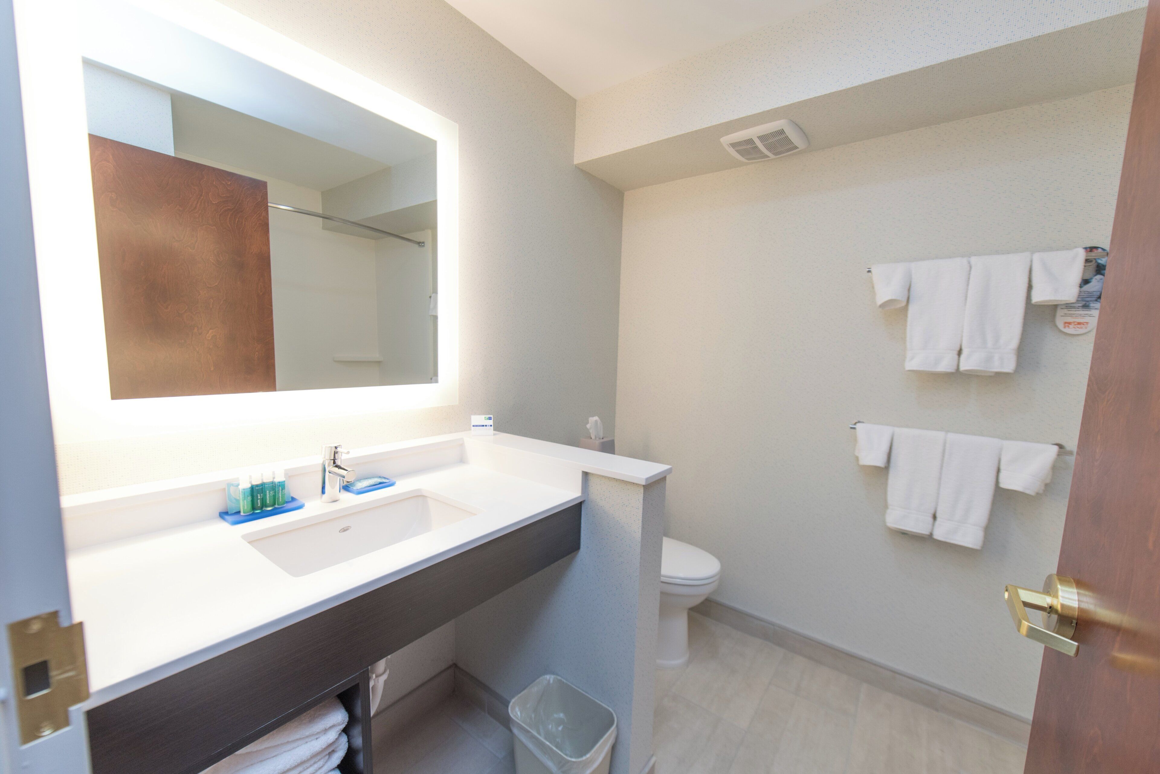 A bathroom with a large mirror, a sink, a toilet, and a trash bin.