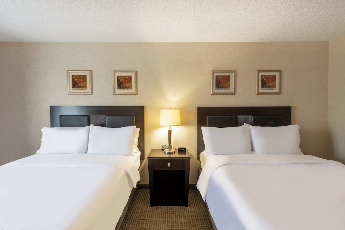 A hotel room with two beds, a nightstand with a lamp, and framed artwork on the wall.