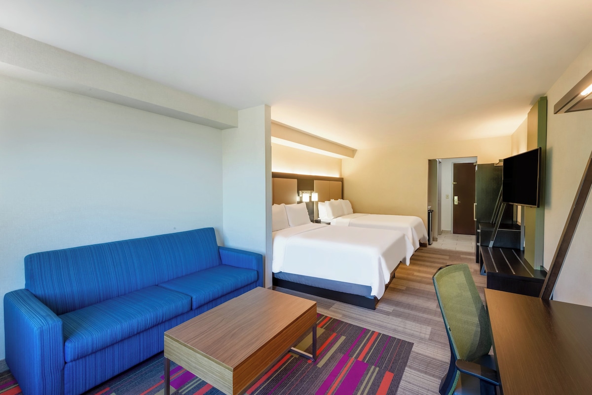 A hotel room with a blue sofa, a wooden coffee table, a bed with white linens, a TV, and a desk.