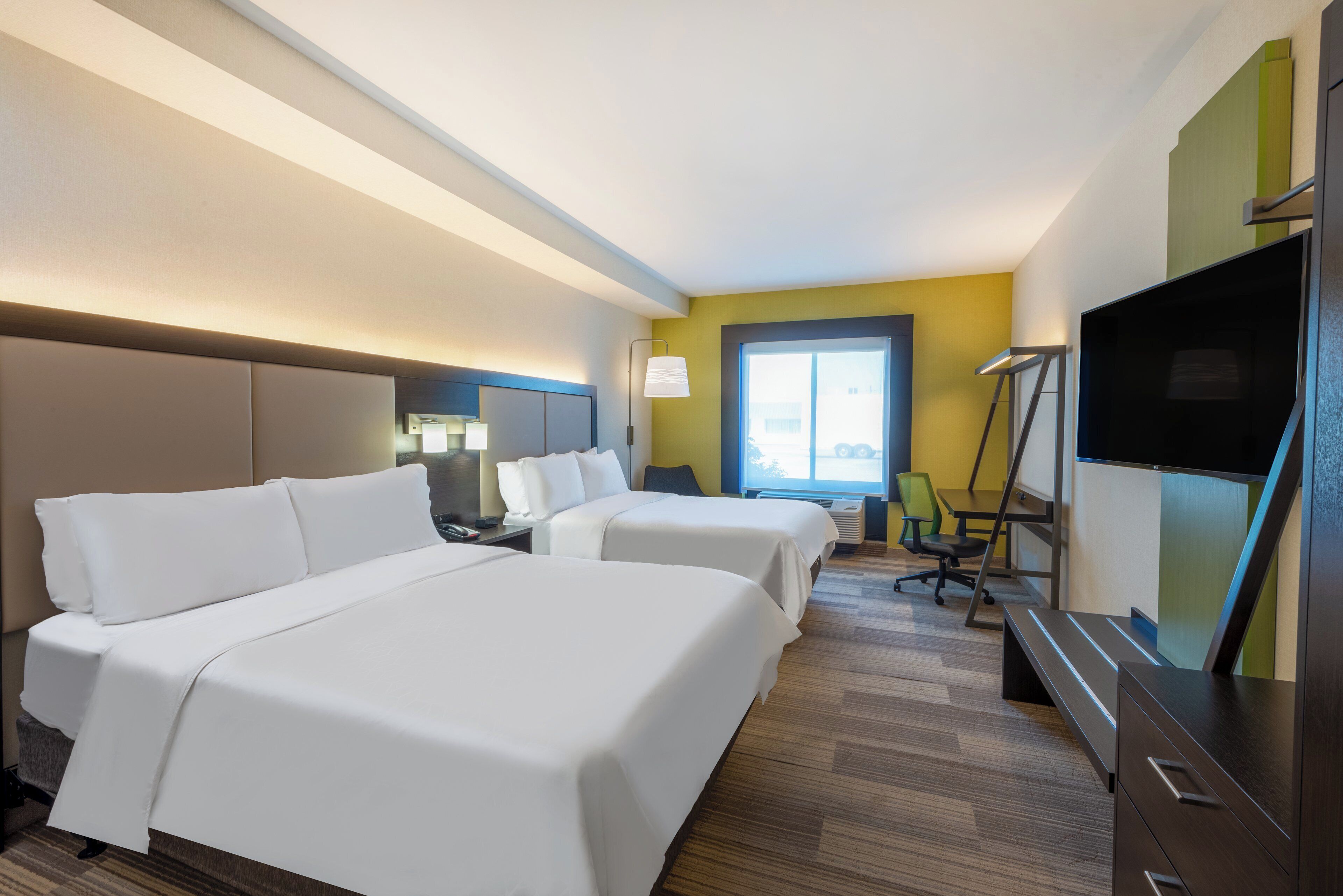 A hotel room with two beds, a desk, a chair, a flat-screen TV, and a window.