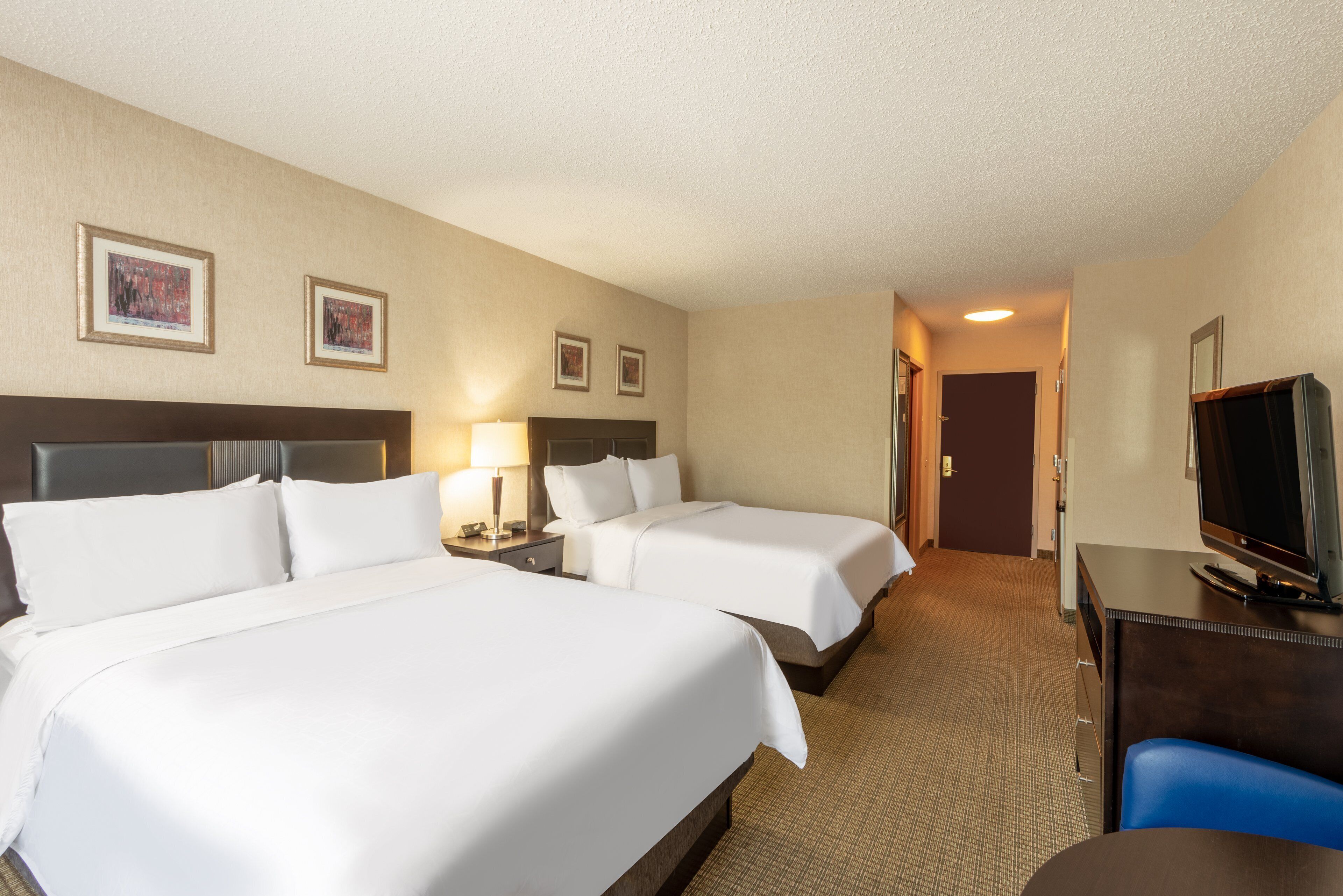 A hotel room with two beds, a desk with a TV, and framed pictures on the wall.