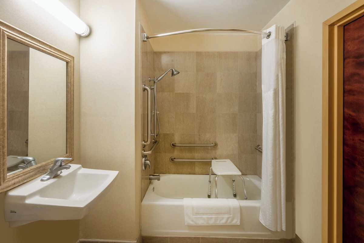 A bathroom with a sink, mirror, bathtub, shower, and grab bars.