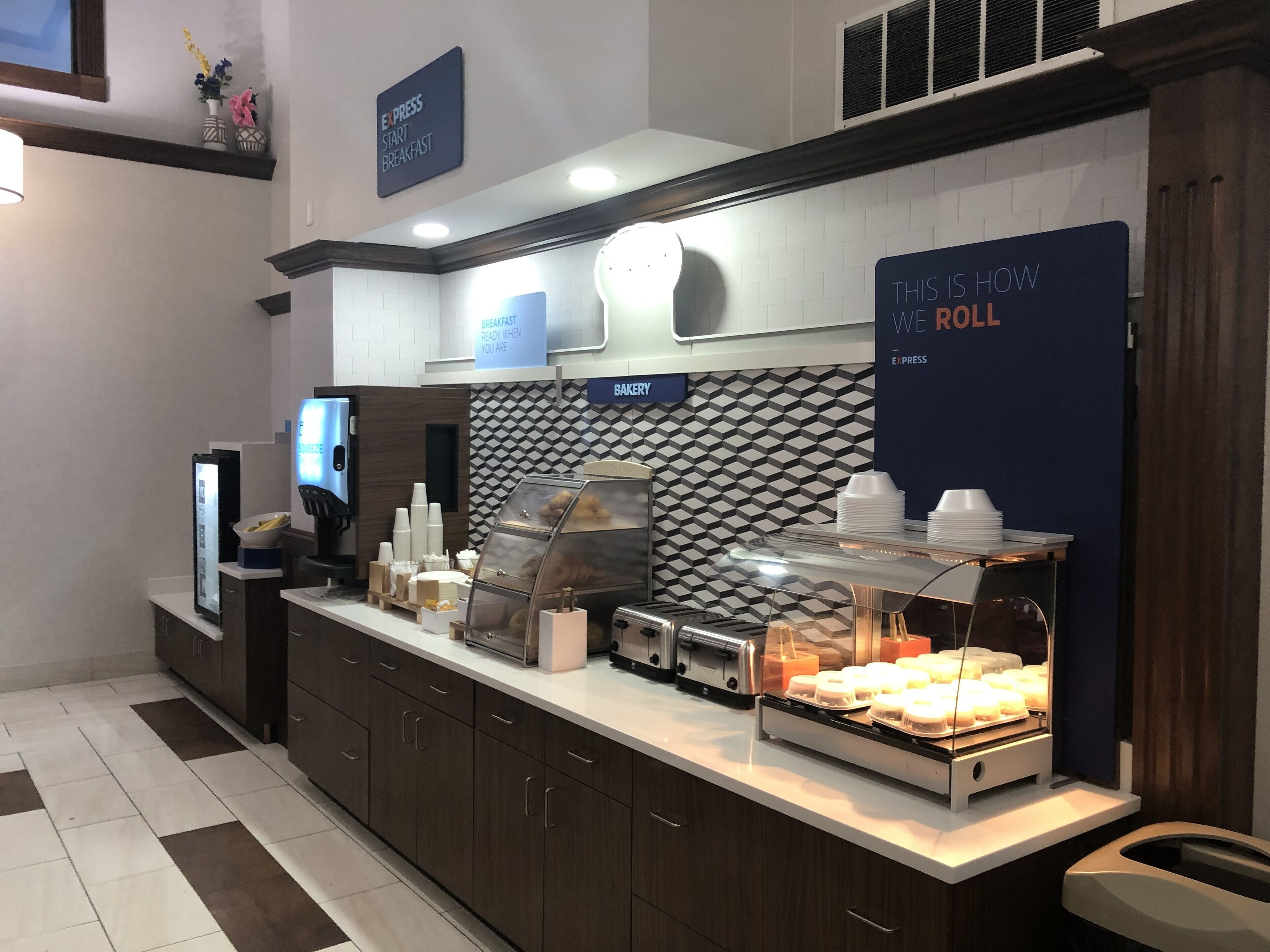 A breakfast area with a bakery display, a digital menu board, and a sign indicating the start of breakfast.