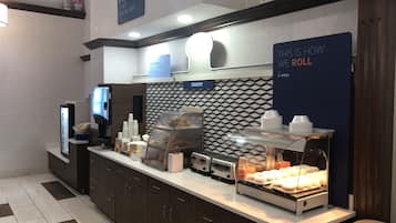 A breakfast area with a bakery display, a digital menu board, and a sign indicating the start of breakfast.