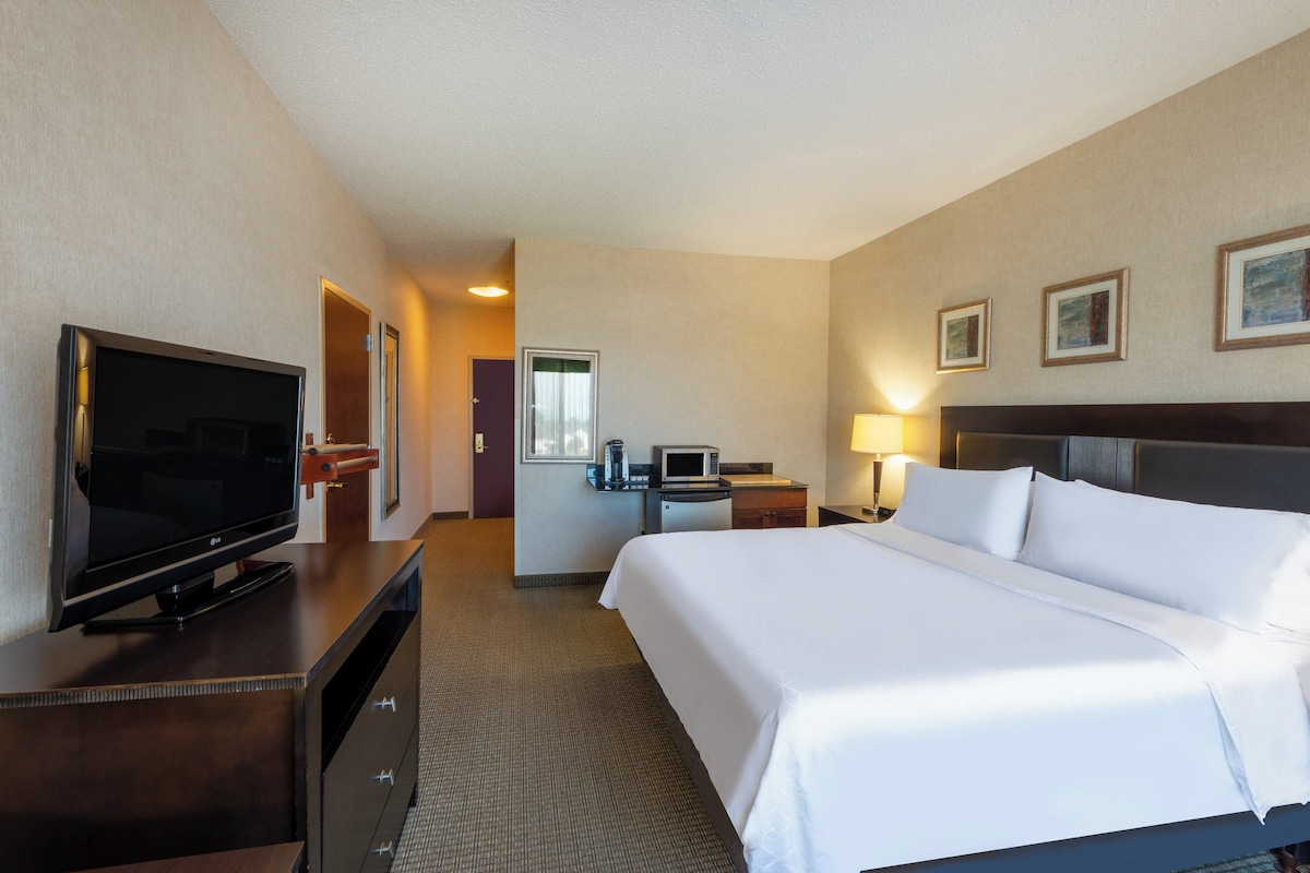 A hotel room with a bed, a TV, a desk with a computer, and a microwave.