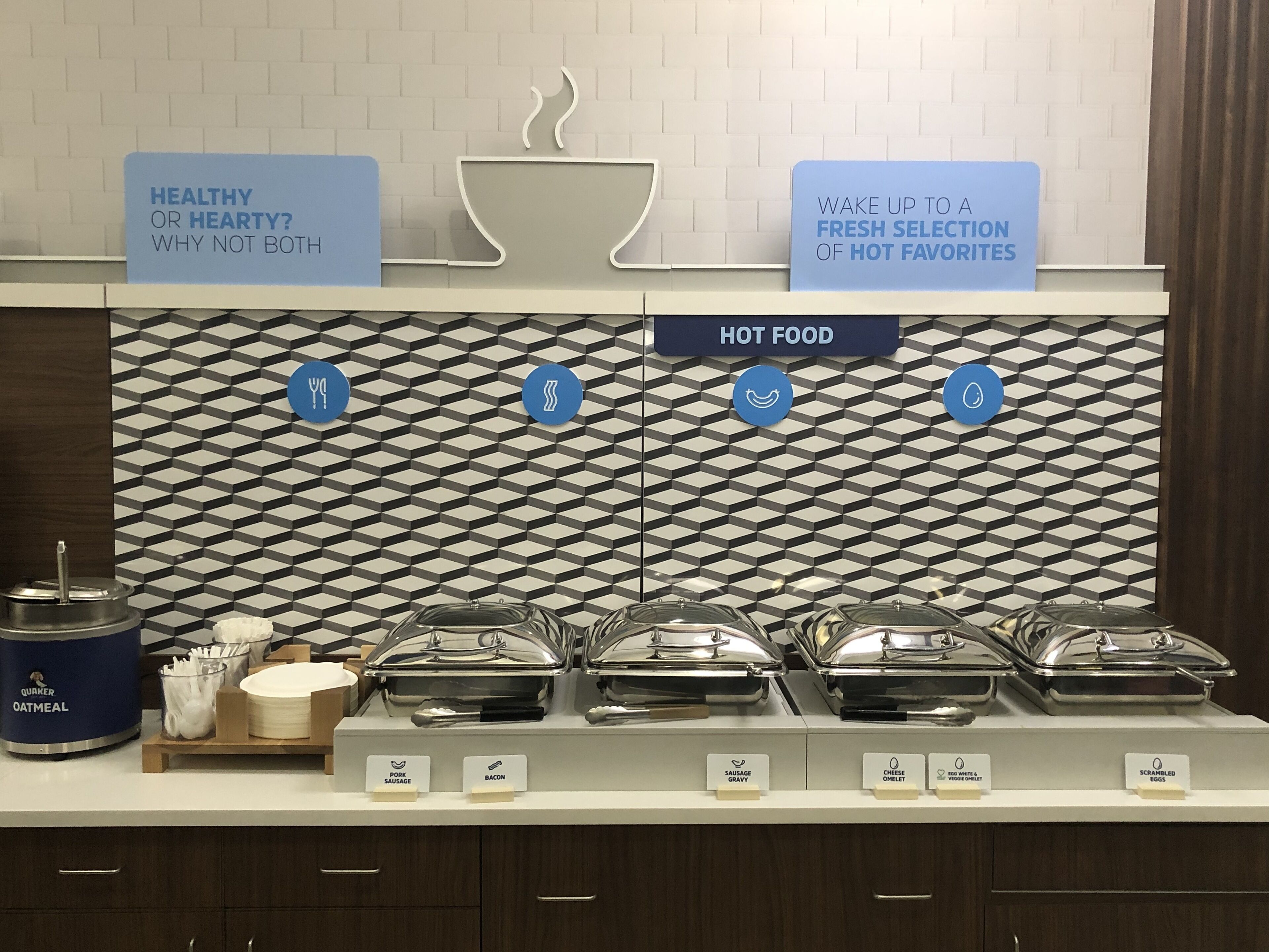 A buffet setup with labeled hot food options including sausage, bacon, and scrambled eggs.