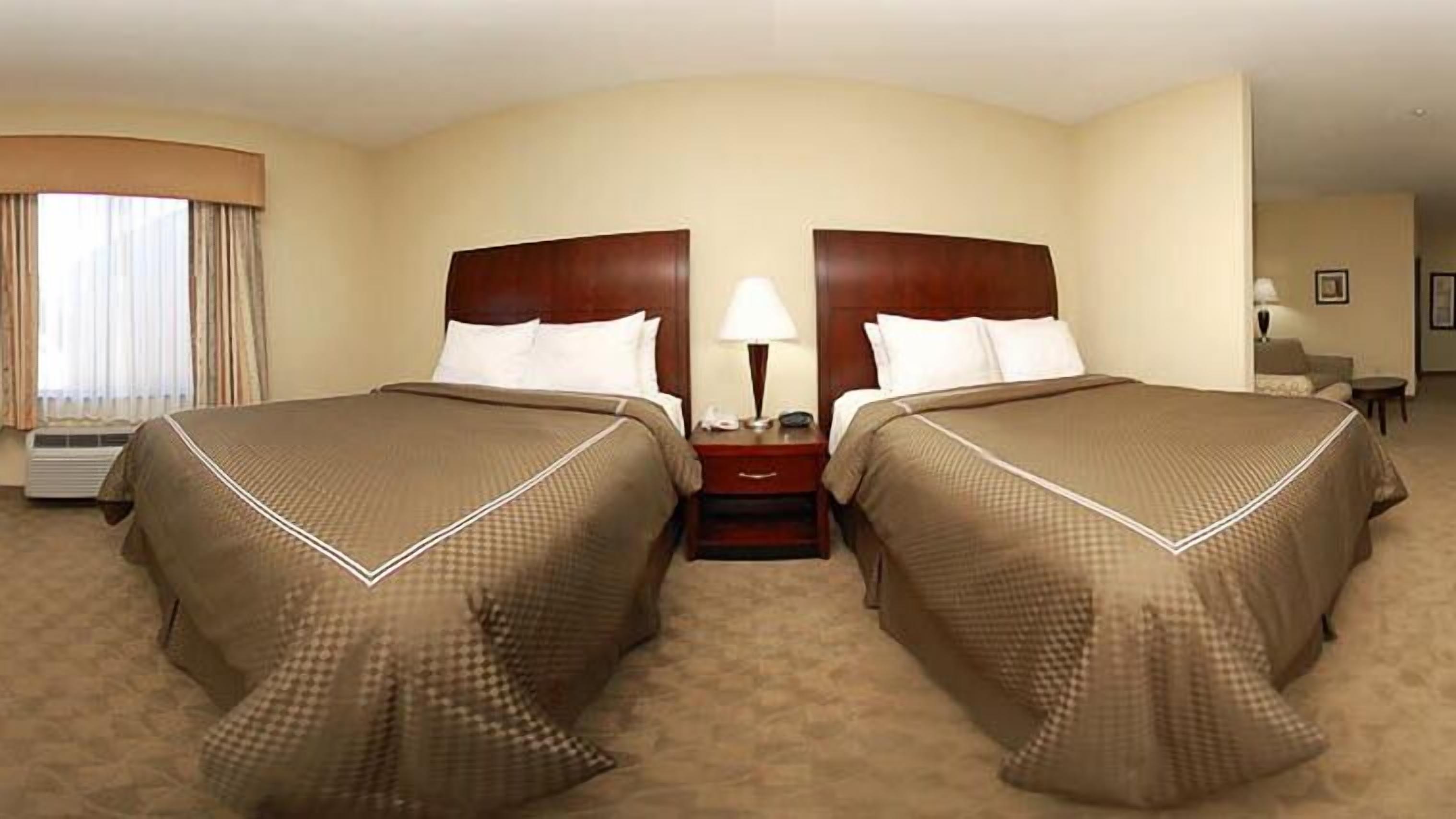 A hotel room with two beds, a nightstand with a lamp, and a window with curtains.