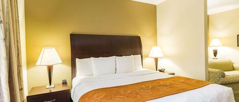 A hotel room with a large bed, two bedside lamps, a nightstand, a chair, and a wall-mounted lamp.
