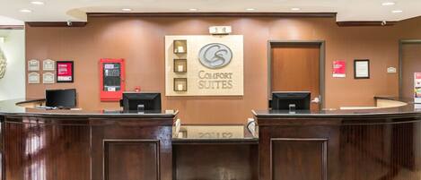 A reception desk with a sign for Comfort Suites, a fire alarm, and a framed certificate on the wall.