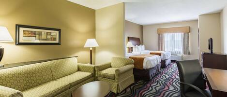 A hotel room with a sofa, armchair, bed, desk, and a patterned carpet.