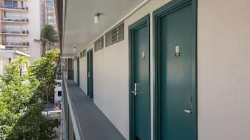 A corridor with teal doors, a balcony, and a view of a tall building with balconies.
