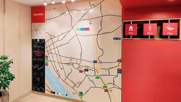 Een hotel lobby met een grote wandkaart, een bordje voor TowneMap, en drie rode borden die zones voor verblijven, werken en ontspanning aangeven.