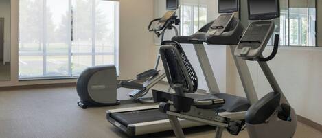 A fitness room with treadmills and an elliptical machine, large windows, and a neutral color scheme.
