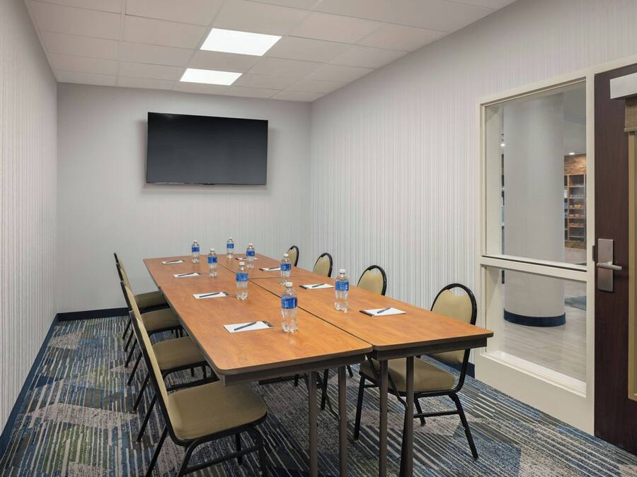A conference room with a long table, chairs, a flat-screen TV, and a carpeted floor.