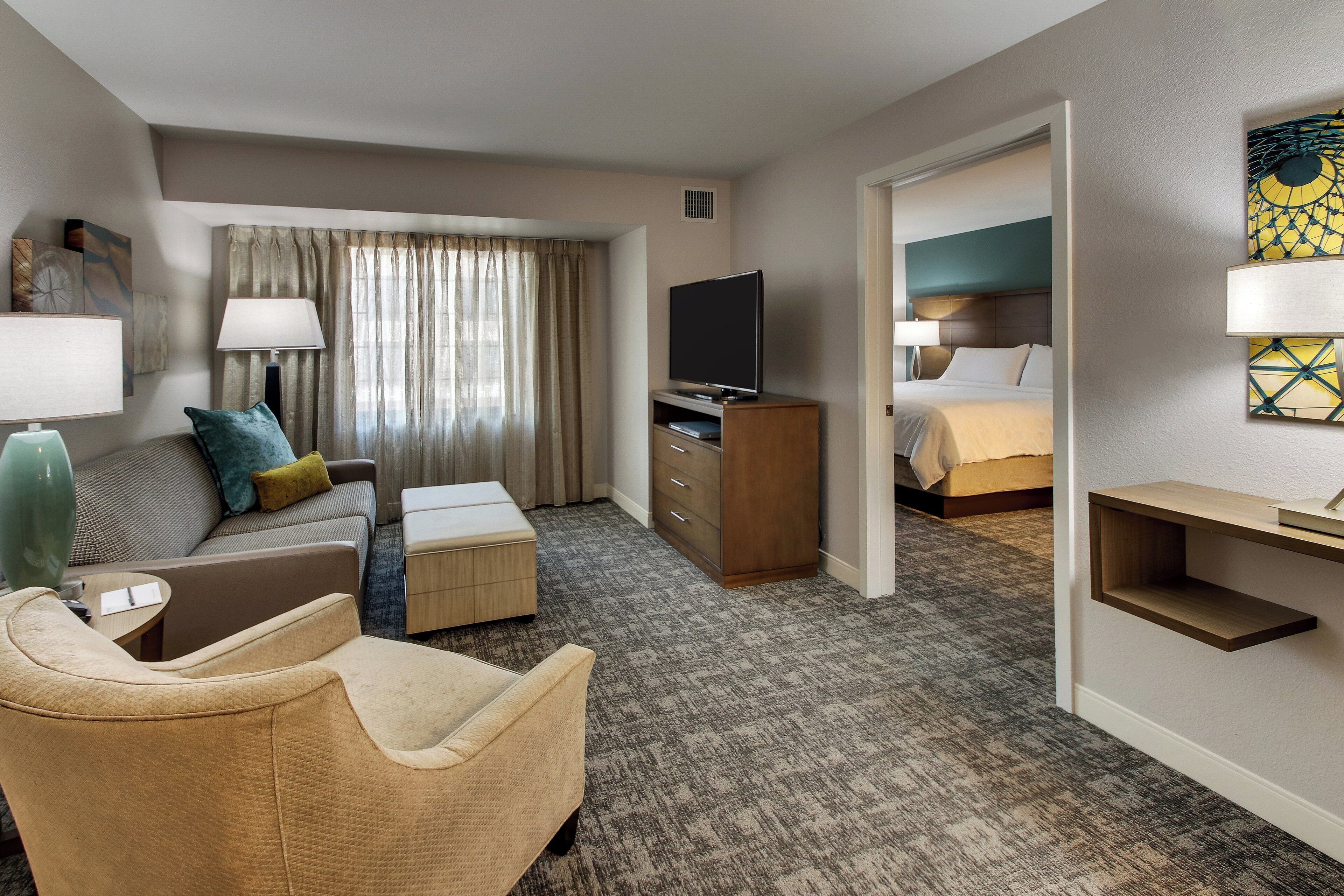 A hotel room with a sofa, a chair, a television, a bed, and a desk.