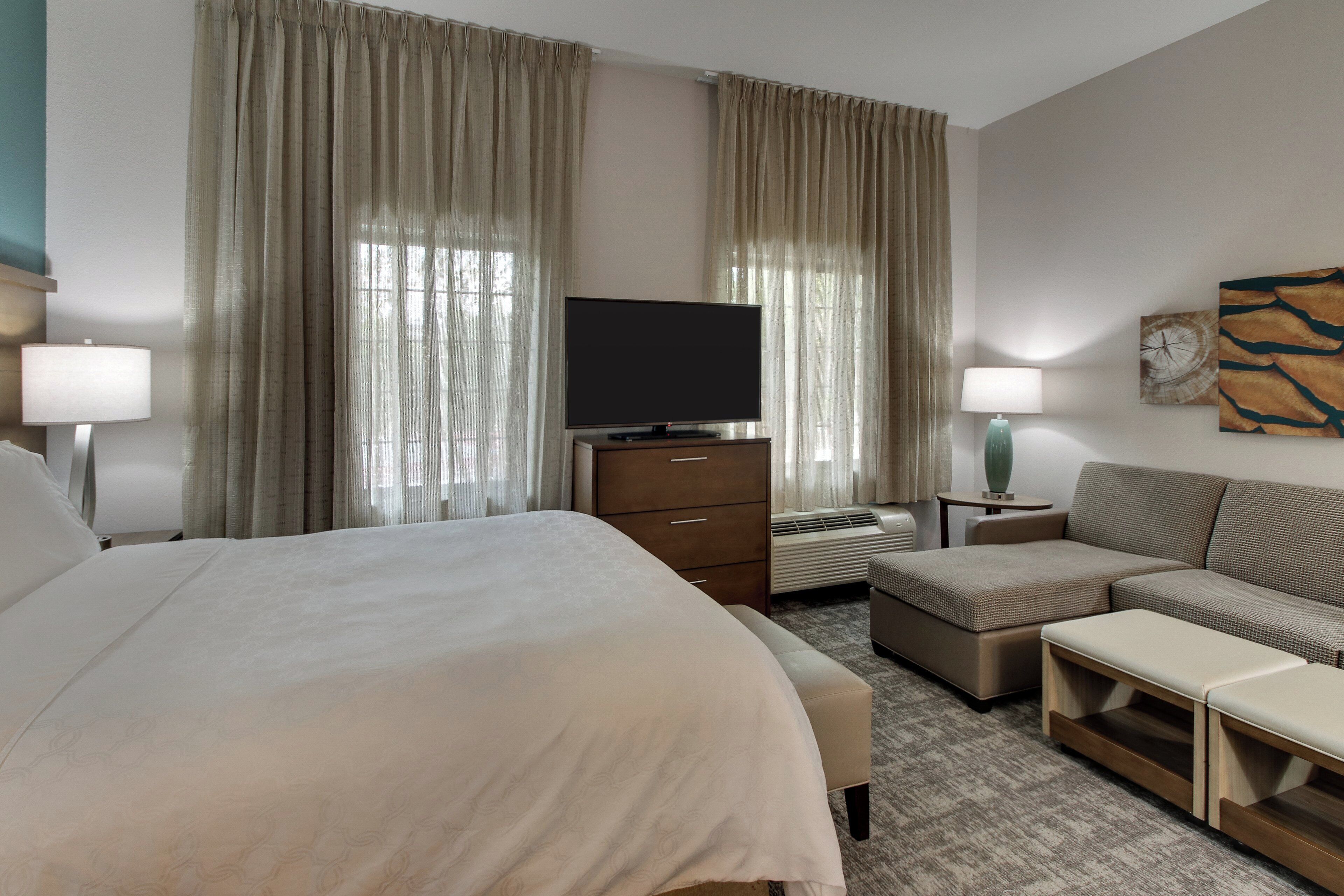 Ein Hotelzimmer mit Bett, Fernseher, Sofa und Schreibtisch mit Lampe.