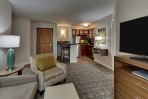 A compact living space with a sofa, a coffee table, a TV, a kitchen area with a refrigerator, microwave, and cabinets, and a dining table with chairs. - Staybridge Suites Missoula by IHG (Missoula)